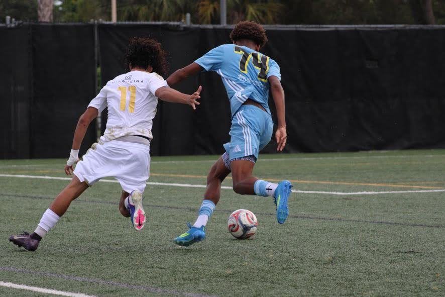 Chaz L. Grey, #74 seen from behind, driving past an opponent in a white kit